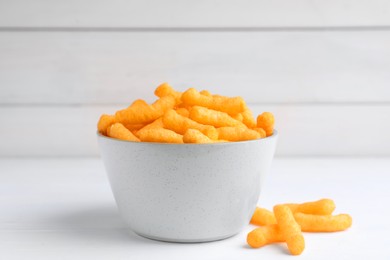 Photo of Bowl with crunchy cheesy corn snack on white table, closeup