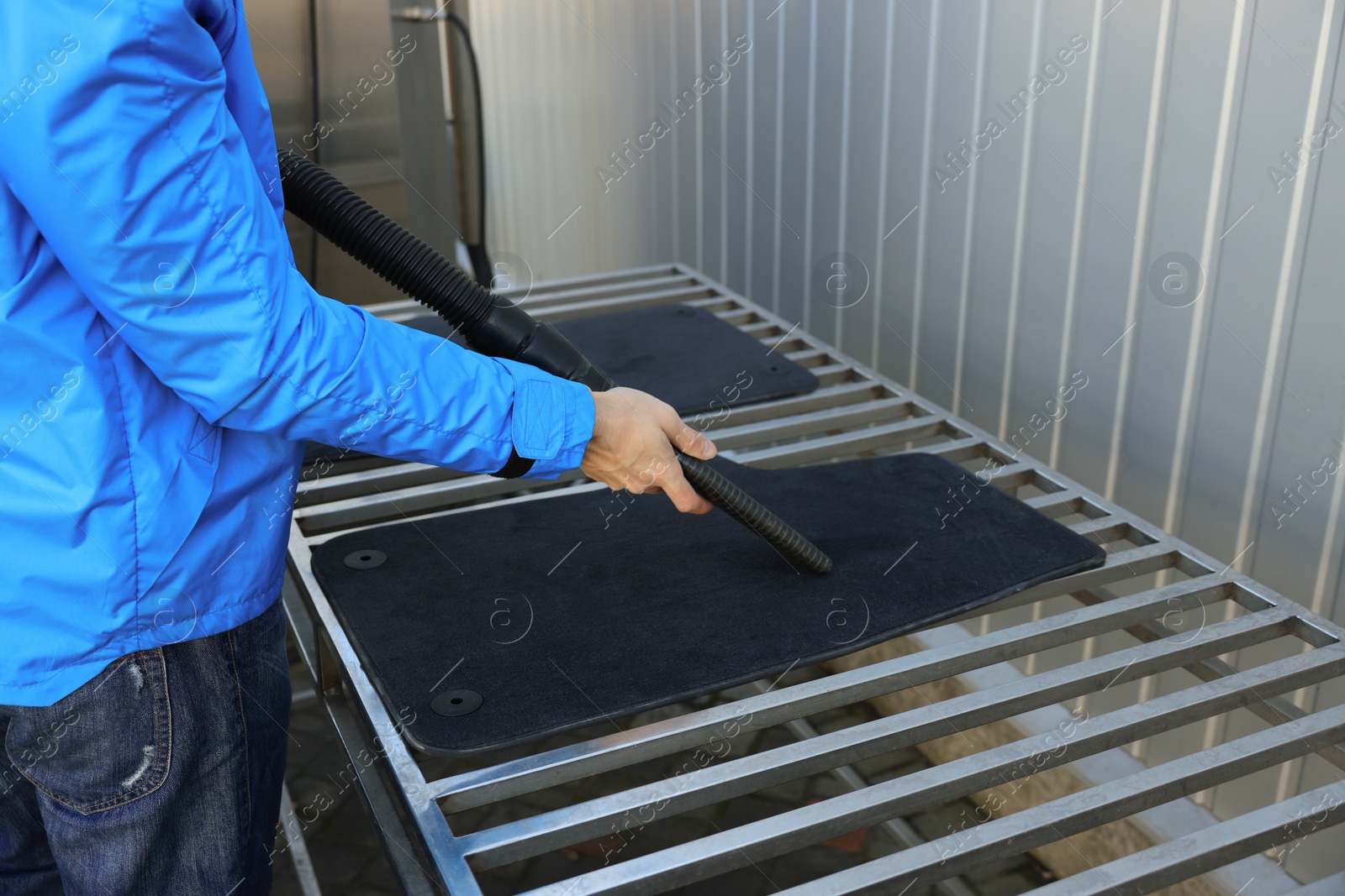 Photo of Man cleaning auto carpets with vacuum cleaner at self-service car wash, closeup