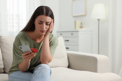 Photo of Stressed woman with credit card and smartphone at home. Be careful - fraud