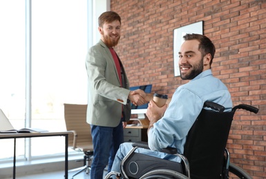 Young man in wheelchair with colleague at office