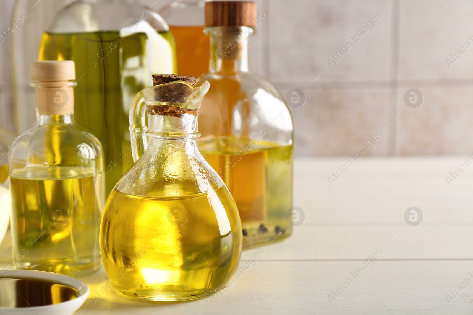 Photo of Vegetable fats. Different oils in glass bottles on white wooden table, closeup. Space for text