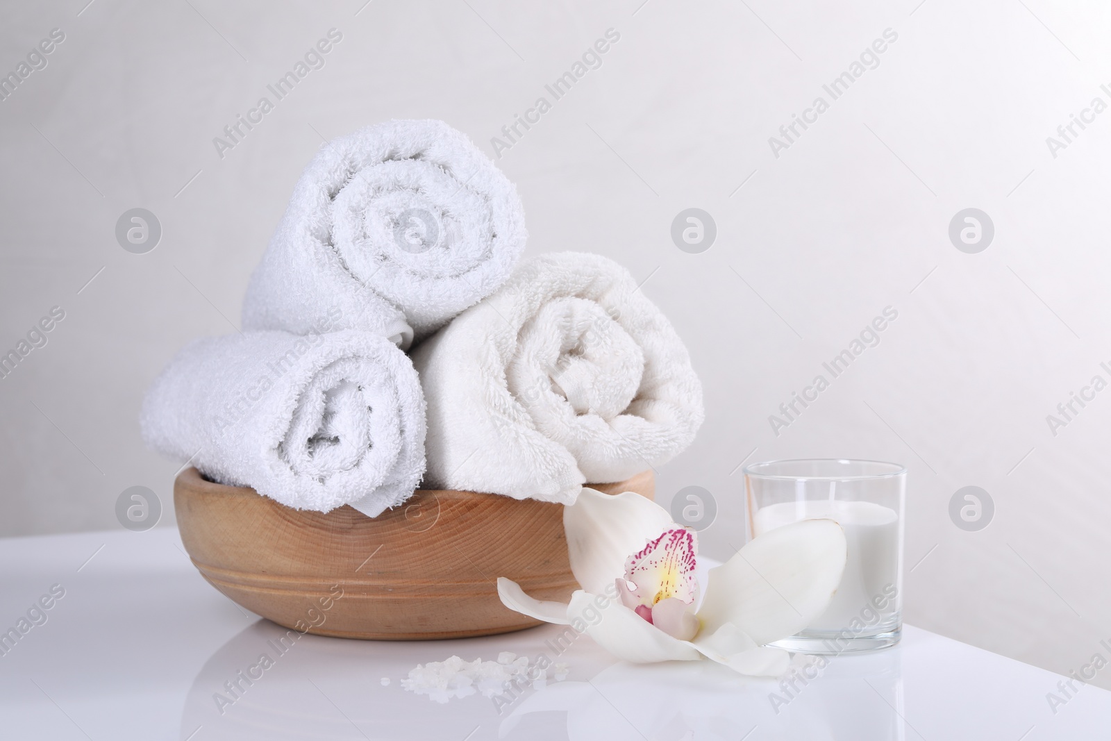 Photo of Spa composition with towels, orchid flower, candle and sea salt on white table