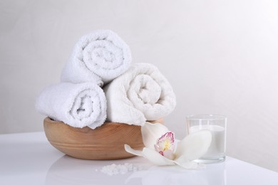 Spa composition with towels, orchid flower, candle and sea salt on white table