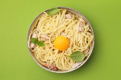 Photo of Bowl of tasty pasta Carbonara with basil leaves on light green background, top view