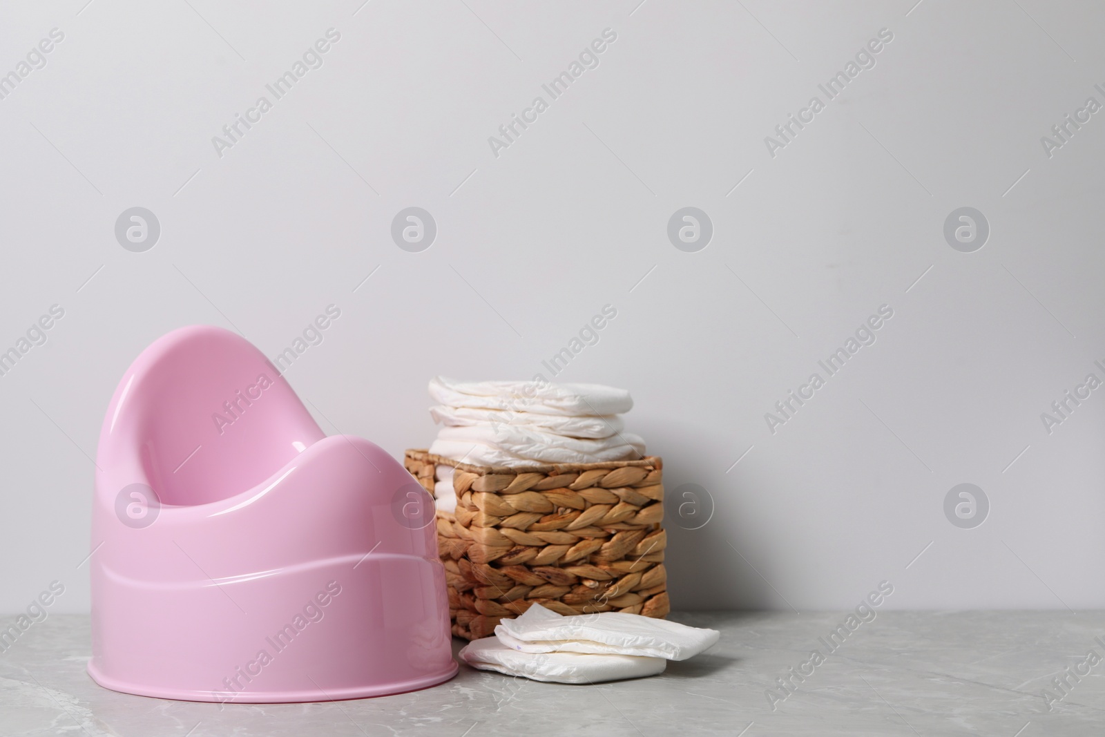 Photo of Pink baby potty and diapers near light wall, space for text. Toilet training