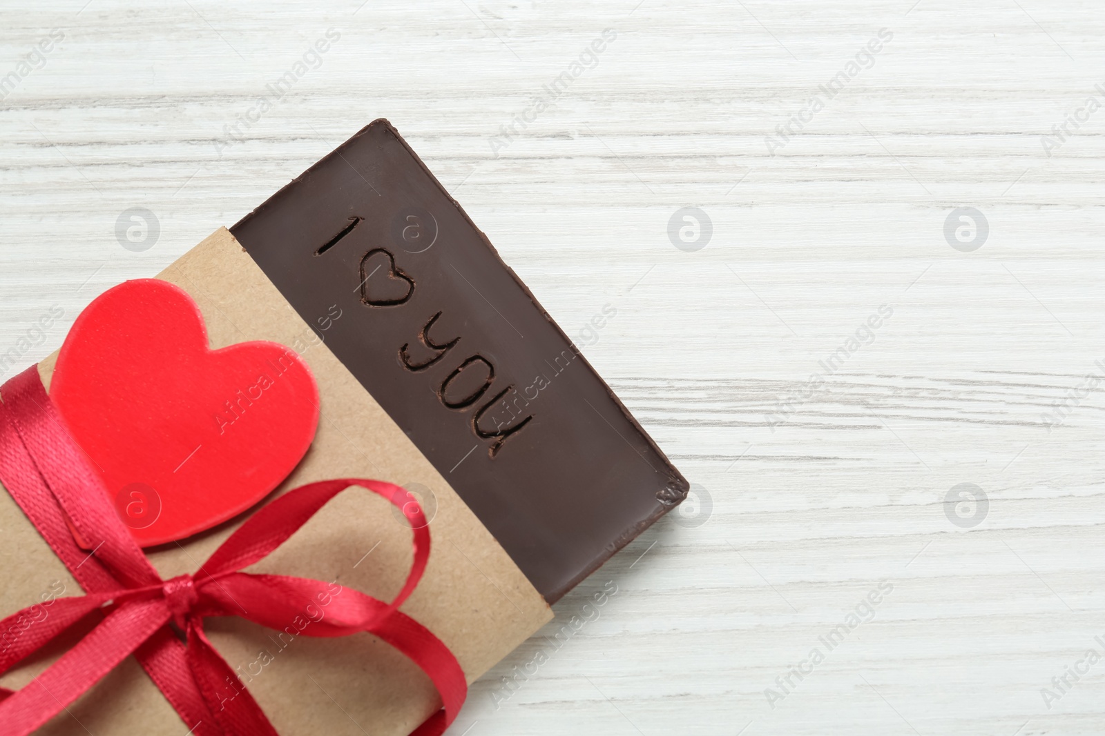 Photo of Chocolate with carved phrase I Love You on white  wooden table, above view