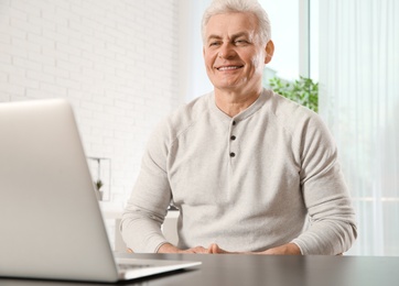 Photo of Mature man using video chat on laptop at home