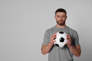 Photo of Athletic young man with soccer ball on light grey background. Space for text