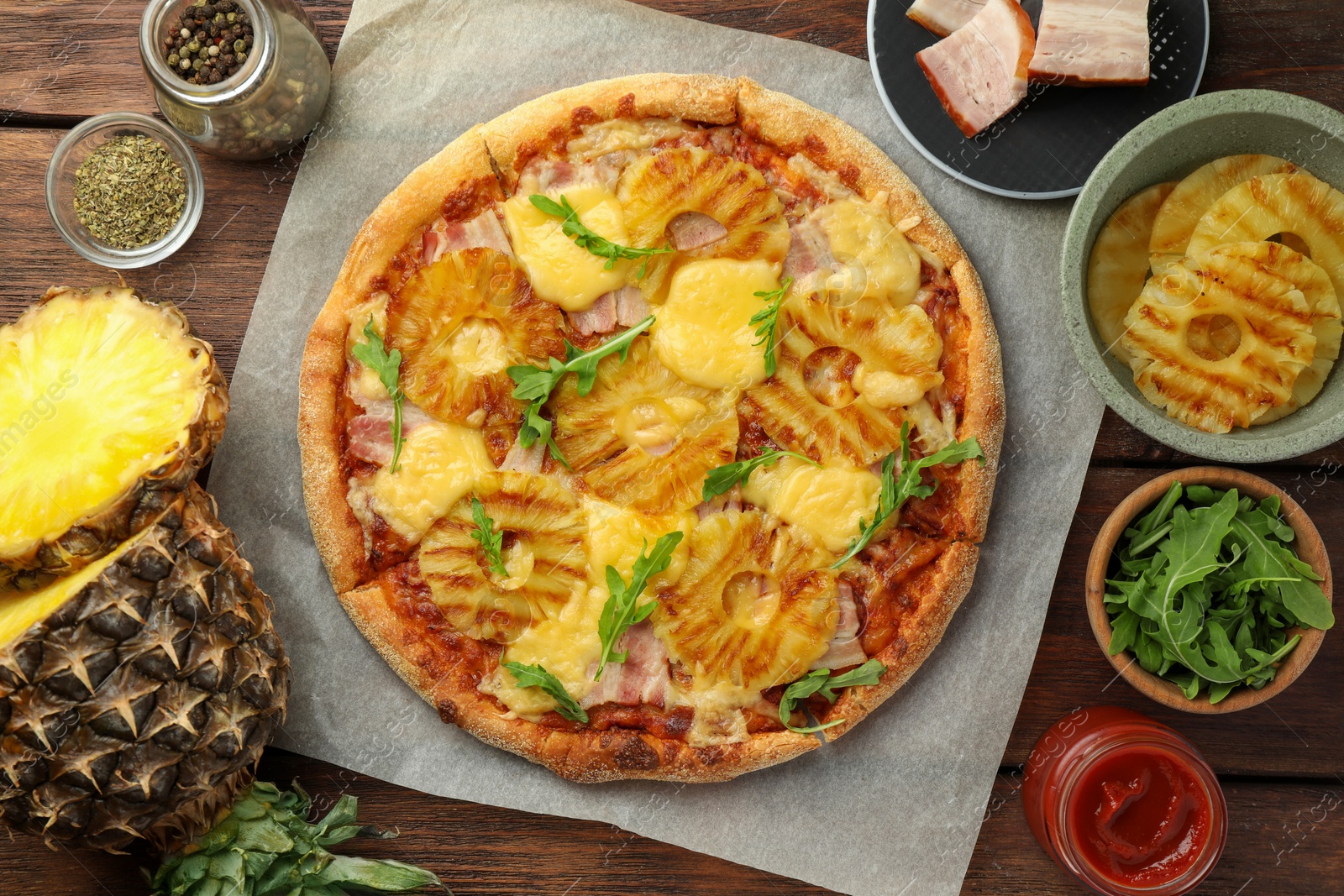 Photo of Delicious pineapple pizza and ingredients on wooden table, flat lay