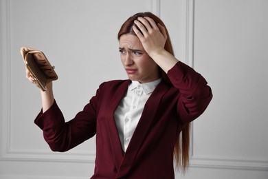 Upset woman with empty wallet near white wall