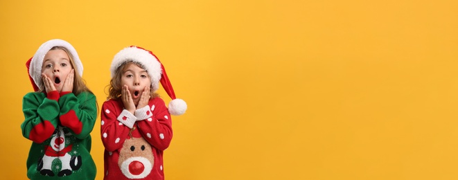 Photo of Kids in Christmas sweaters and Santa hats on yellow background, space for text