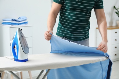 Photo of Man ironing shirt on board at home, closeup