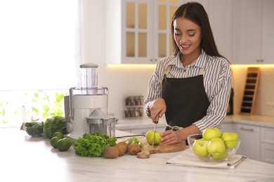 Photo of Young woman cutting fresh apple for juice at table in kitchen