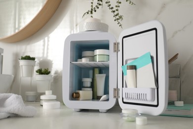 Photo of Cosmetics refrigerator and skin care products on white table indoors