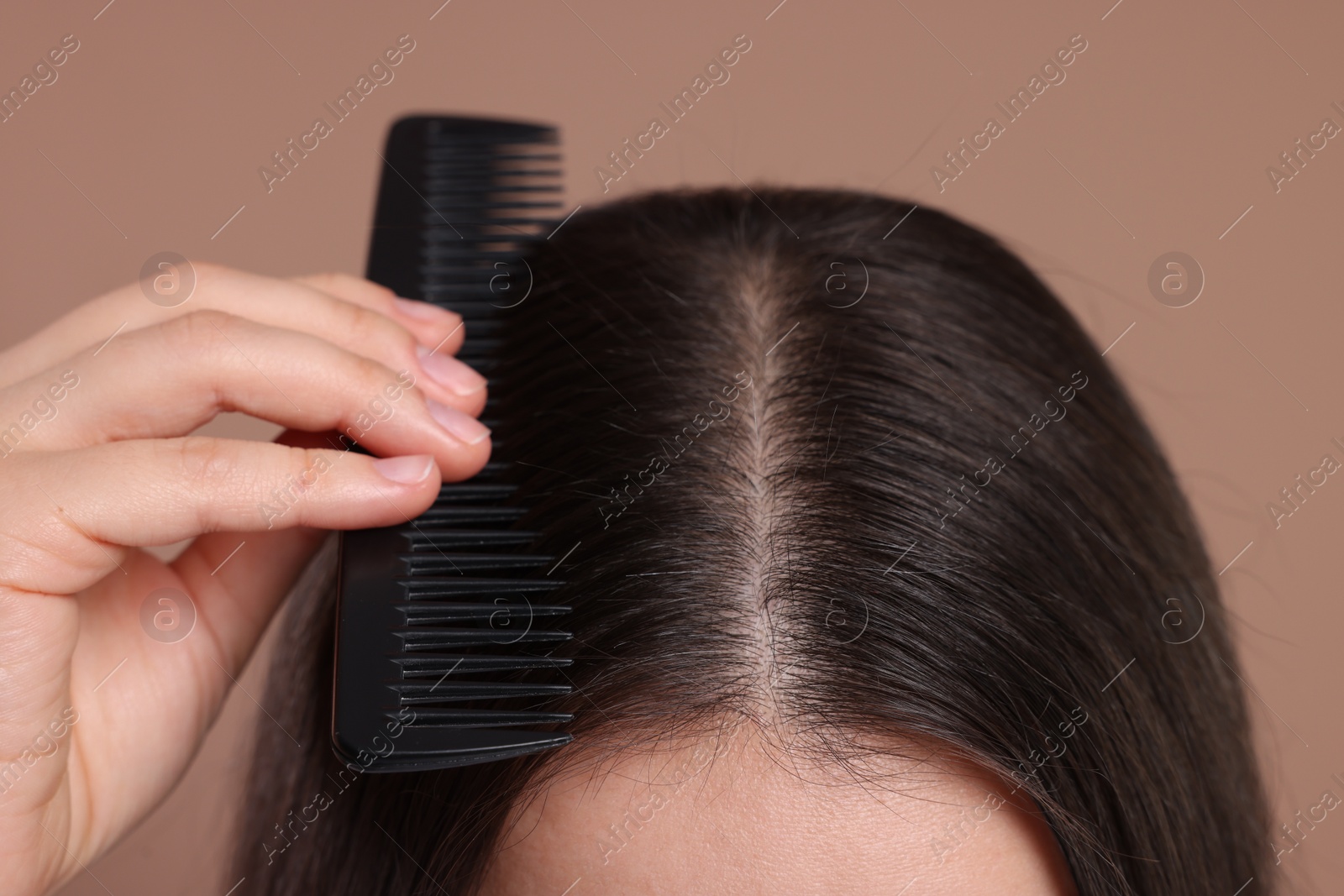 Photo of Woman with comb examining her hair and scalp on beige background, closeup