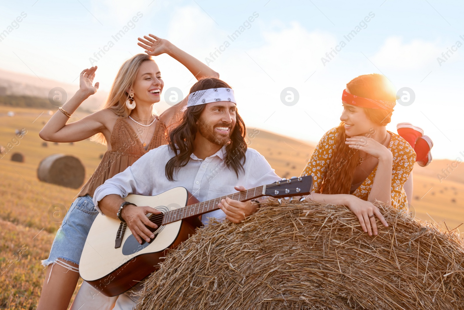 Photo of Beautiful hippie women listening to their friend playing guitar in field