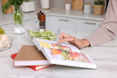 Photo of Woman with recipe book at table in kitchen, closeup