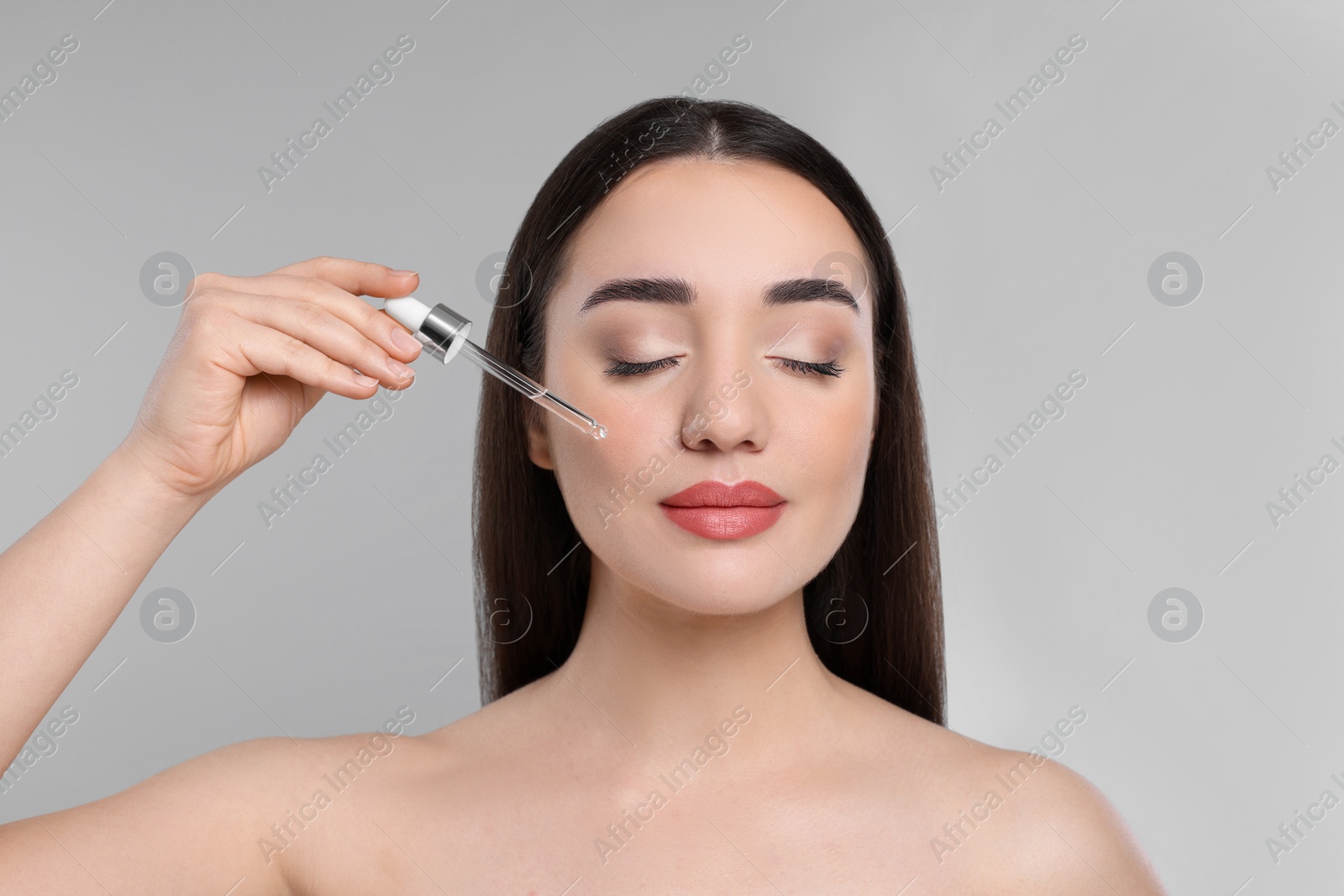 Photo of Young woman applying essential oil onto face on light grey background