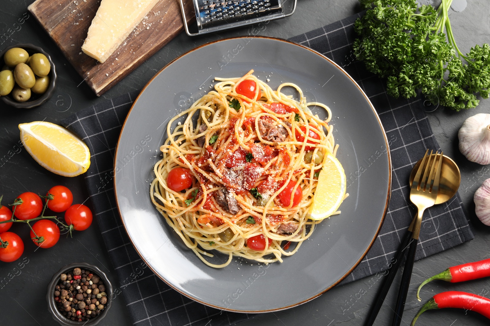Photo of Plate of delicious pasta with anchovies, tomatoes and parmesan cheese near ingredients on black table, flat lay