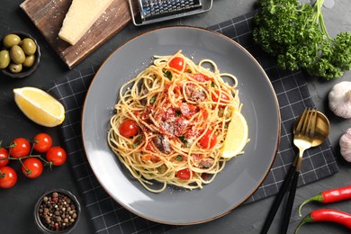 Photo of Plate of delicious pasta with anchovies, tomatoes and parmesan cheese near ingredients on black table, flat lay