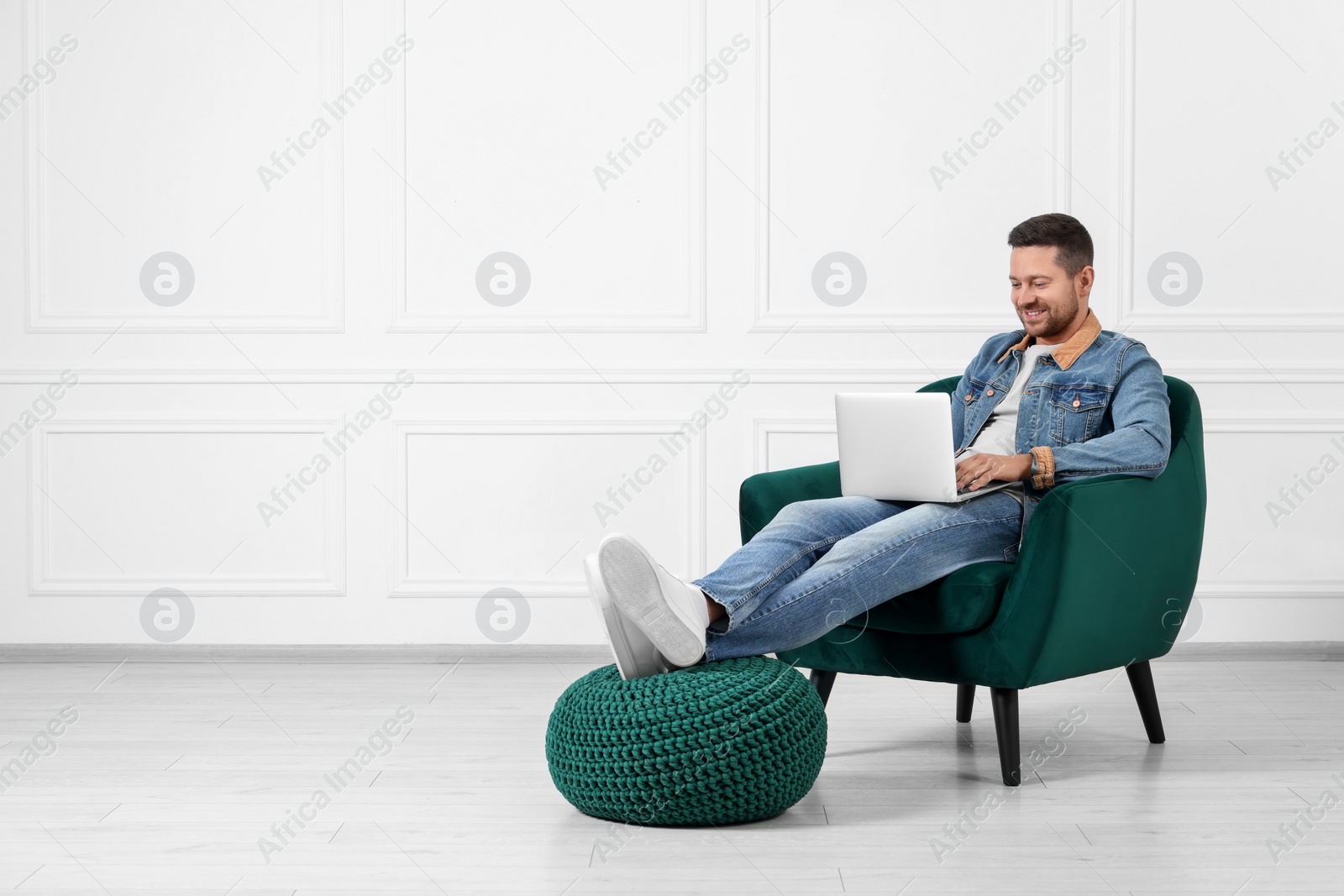 Photo of Happy man sitting in armchair and using laptop indoors, space for text