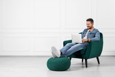 Happy man sitting in armchair and using laptop indoors, space for text