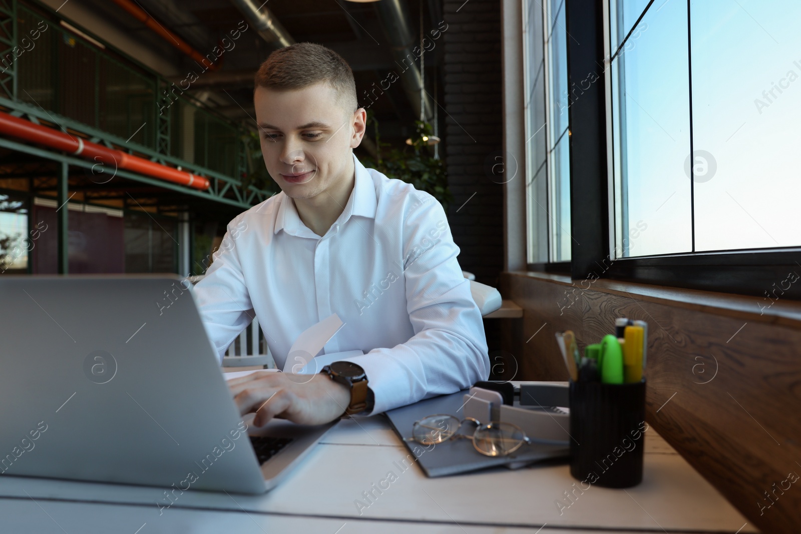 Photo of Young male student with laptop studying at table in cafe