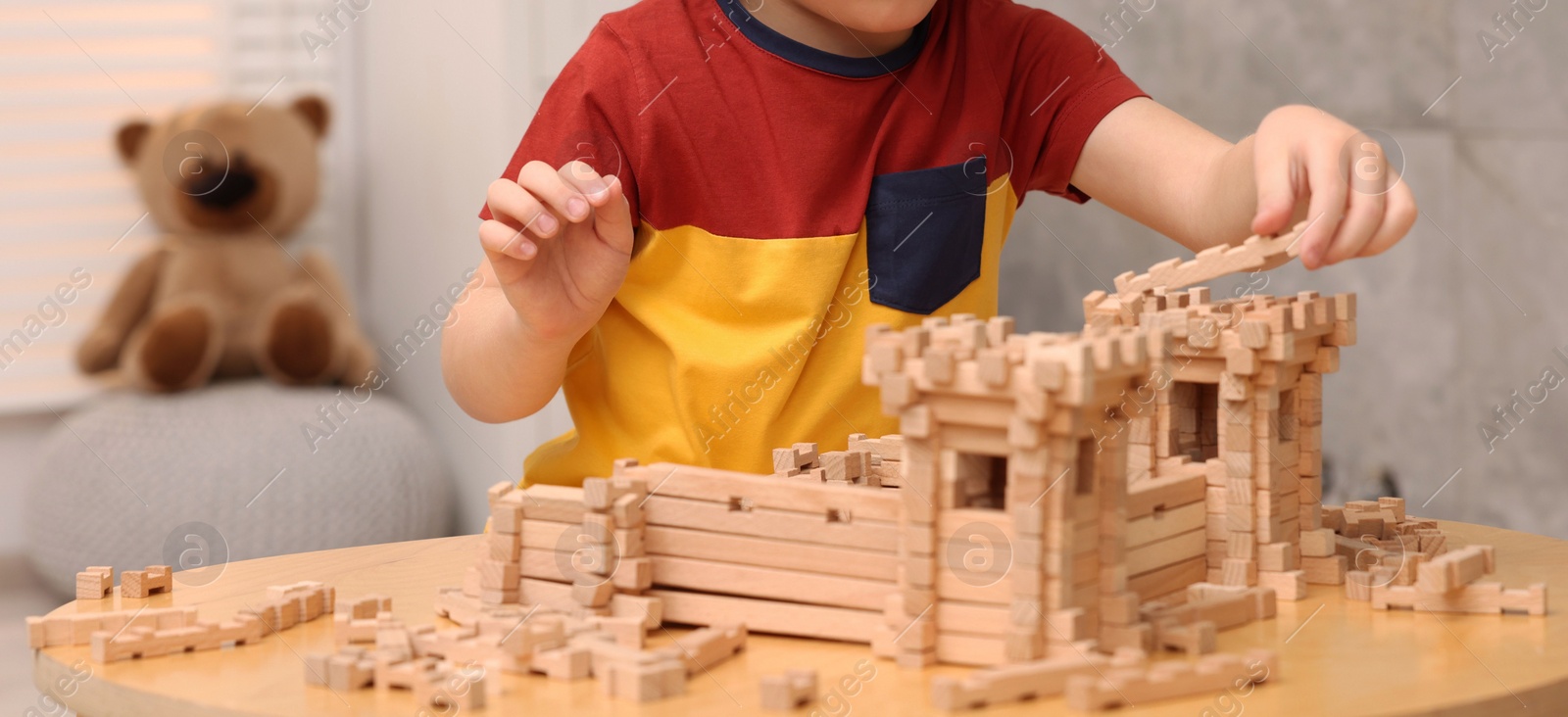 Photo of Little boy playing with wooden construction set at table in room, closeup. Child's toy