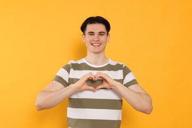 Photo of Happy volunteer making heart with his hands on orange background