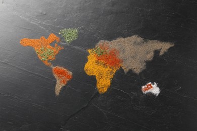 Photo of World map of different spices on dark textured table, flat lay