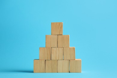 Photo of Pyramid of blank wooden cubes on light blue background