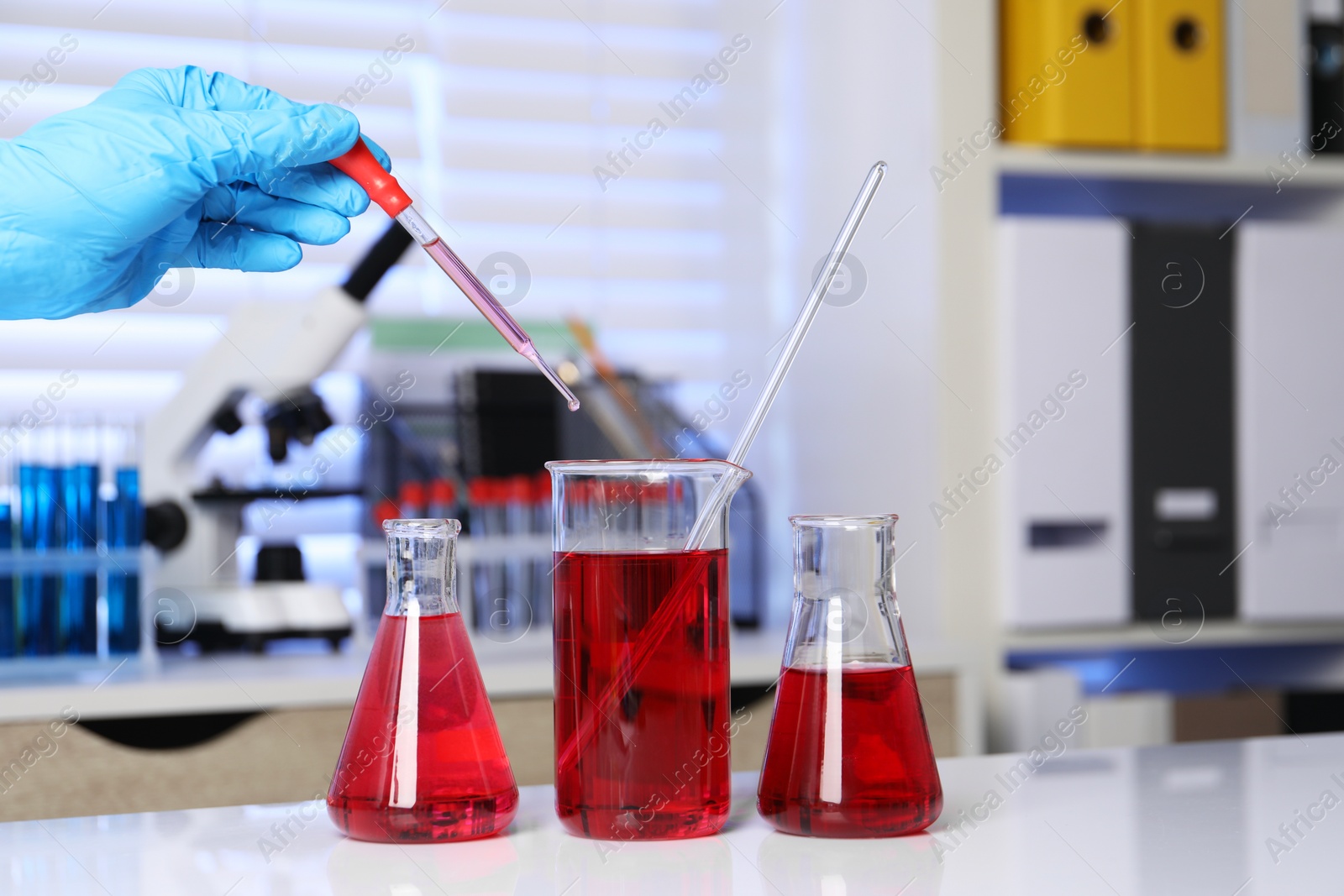 Photo of Laboratory analysis. Woman dripping red liquid into beaker on white table, closeup