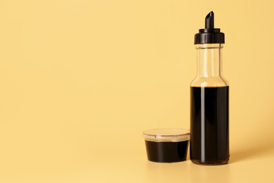 Bottle and bowl with soy sauce on yellow background, space for text