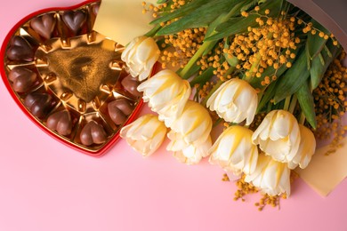 Bouquet with beautiful tulips, mimosa flowers and box of chocolate candies in shape of heart on pink background, flat lay