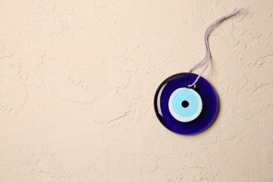 Photo of Evil eye amulet on beige textured table, top view. Space for text