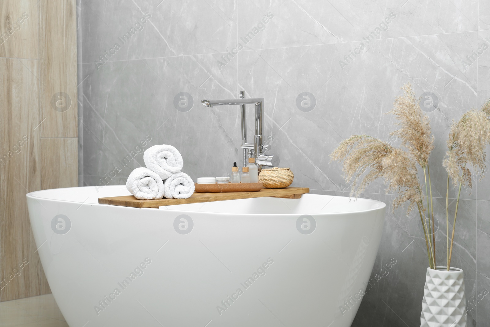 Photo of Rolled bath towels and personal care products on tub tray in bathroom