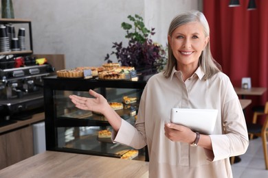 Photo of Happy business owner with tablet inviting to come into her cafe