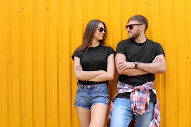 Photo of Young couple wearing black t-shirts near color wall on street