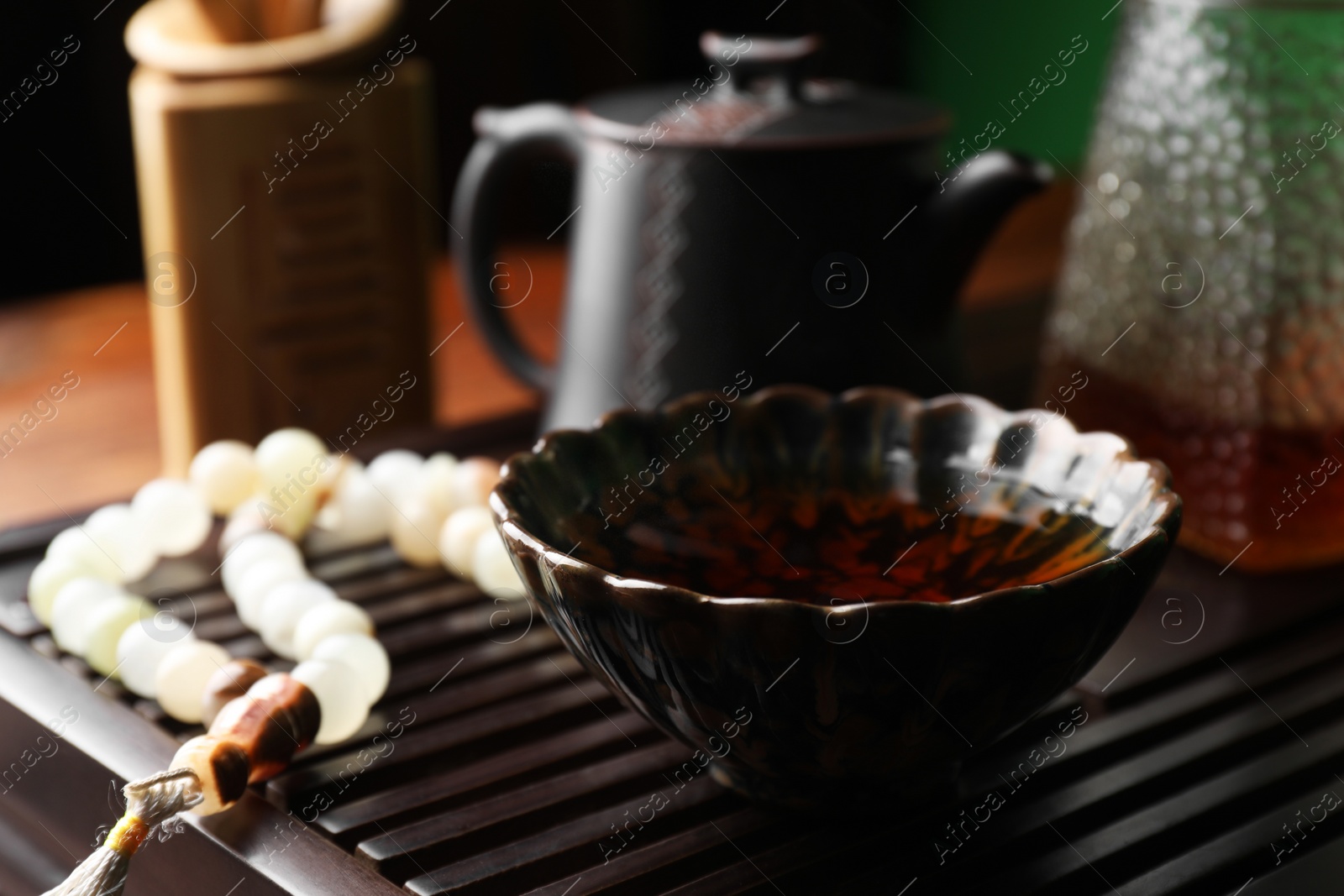 Photo of Cup with freshly brewed pu-erh tea and prayer beads on wooden tray, closeup