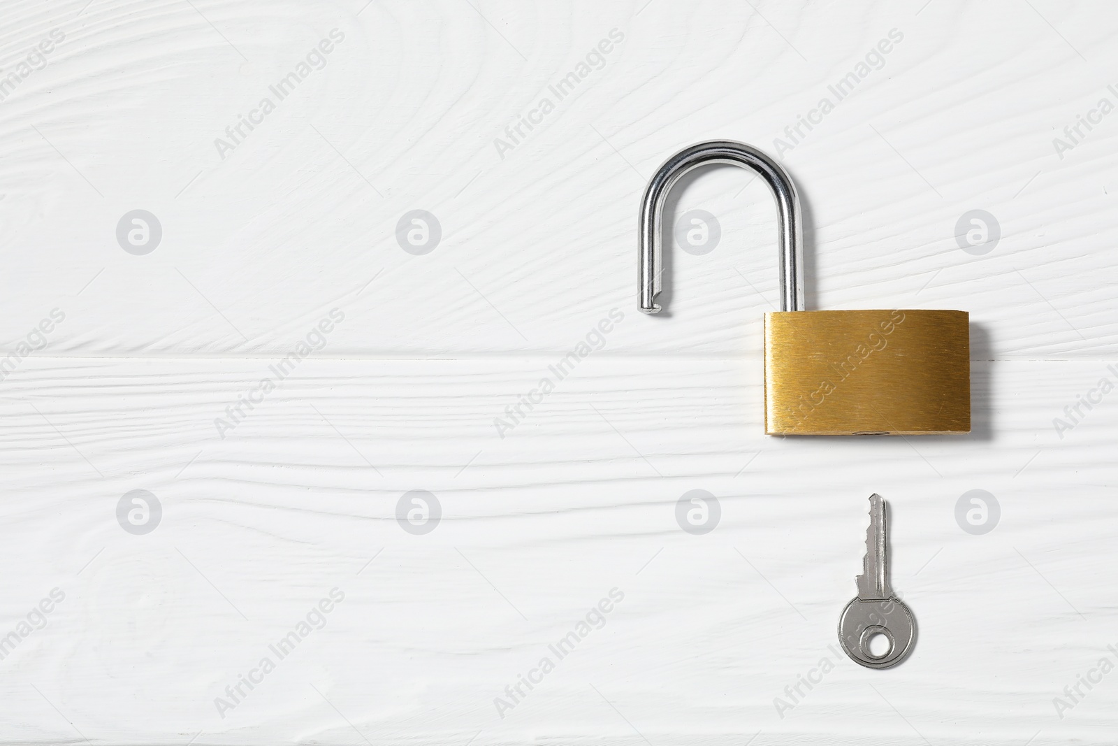 Photo of Steel padlock with key on white wooden table, top view. Space for text