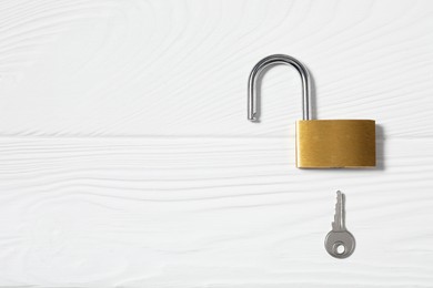 Photo of Steel padlock with key on white wooden table, top view. Space for text