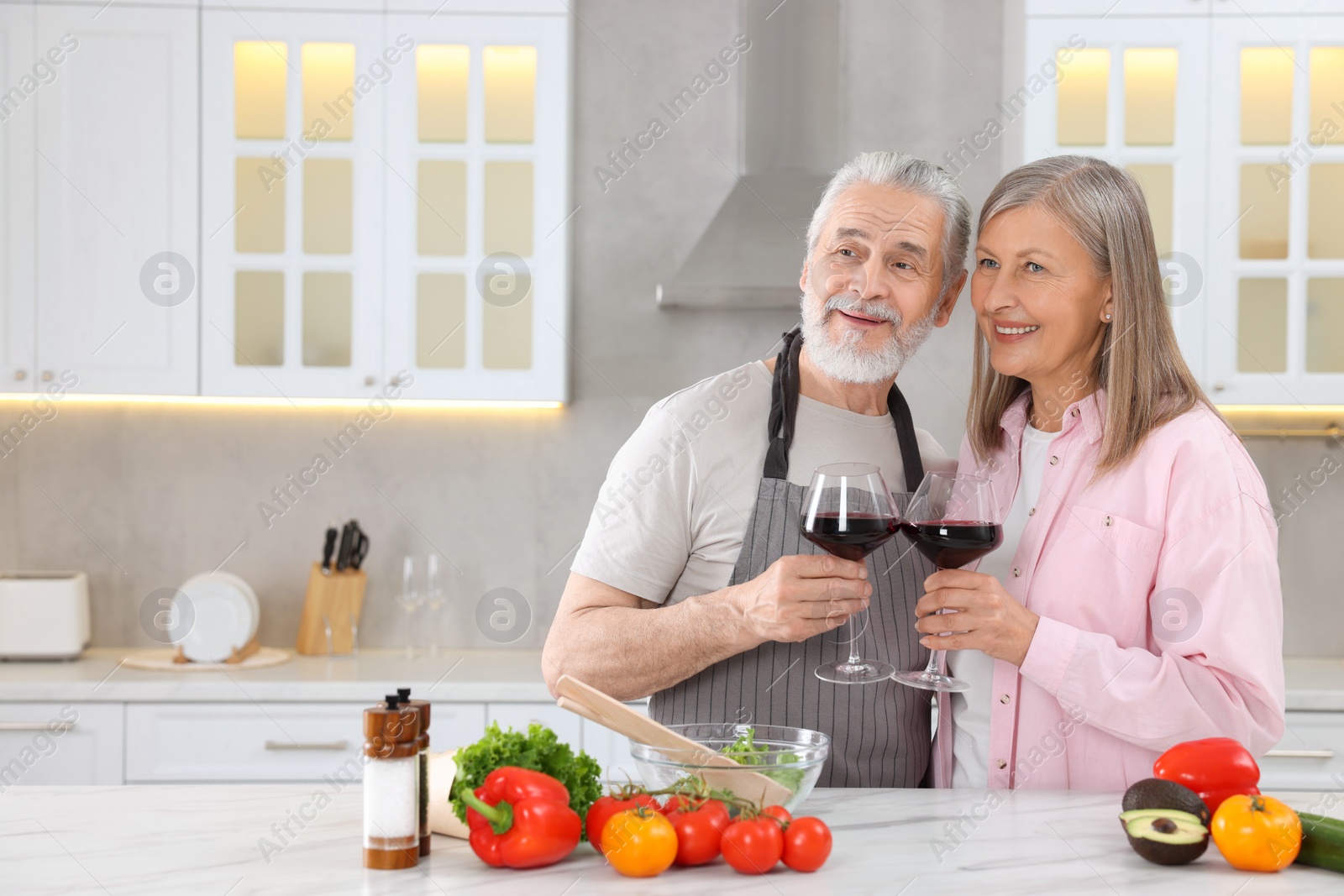 Photo of Happy affectionate senior couple with glasses of wine in kitchen