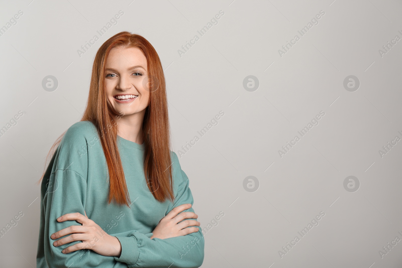 Photo of Candid portrait of happy young woman with charming smile and gorgeous red hair on light background, space for text