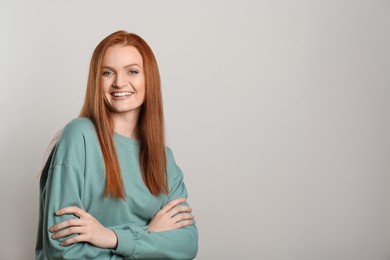 Candid portrait of happy young woman with charming smile and gorgeous red hair on light background, space for text