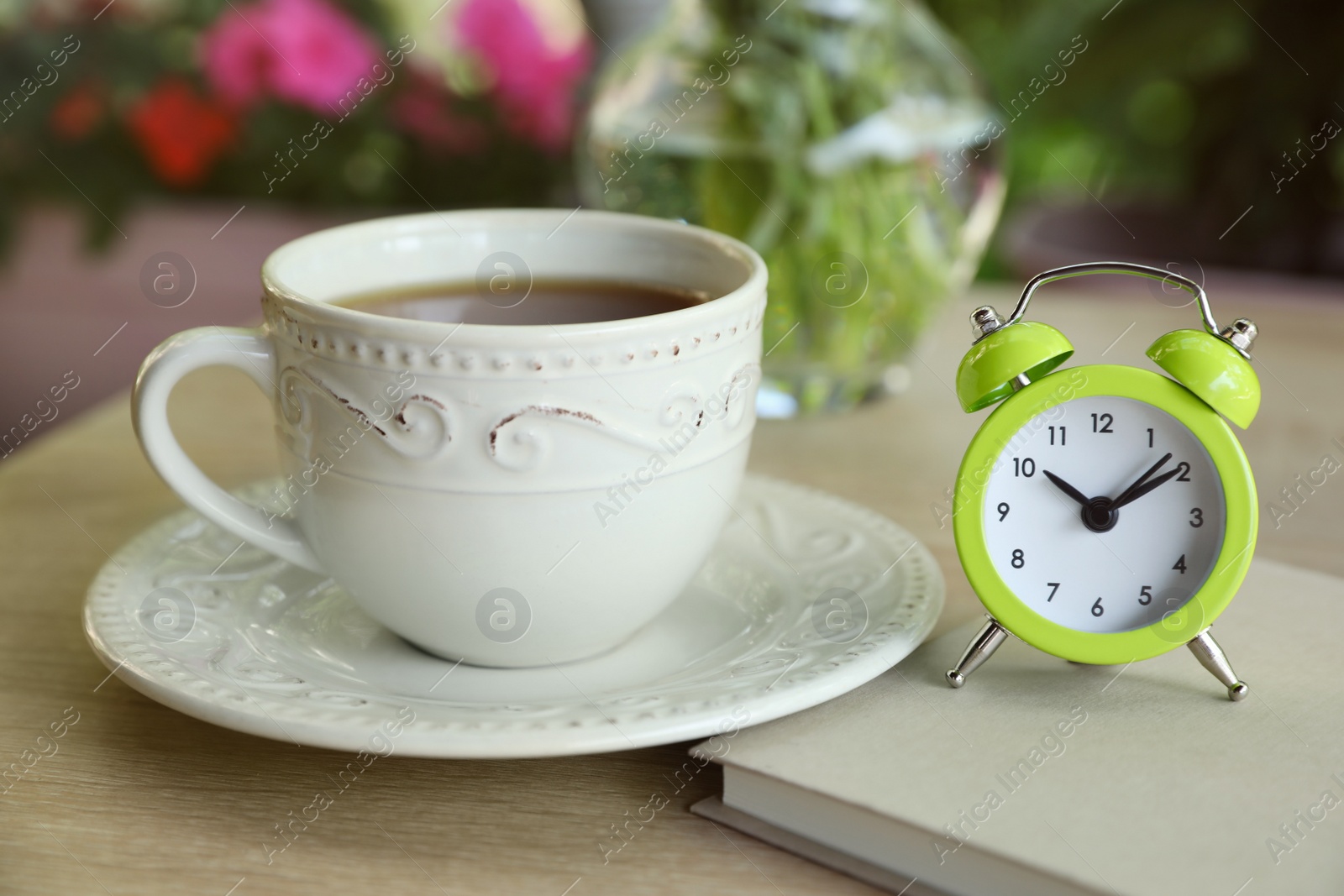 Photo of Cup of drink, alarm clock and notebook on table outdoors in morning