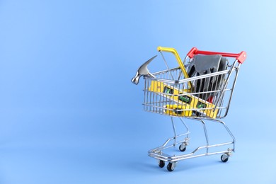 Photo of Small shopping cart with set of construction tools and gloves on light blue background. Space for text