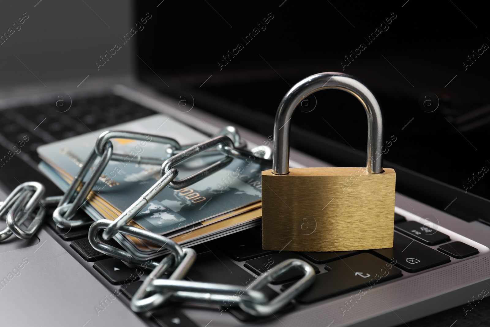 Photo of Cyber security. Metal padlock, chain and credit cards on laptop, closeup