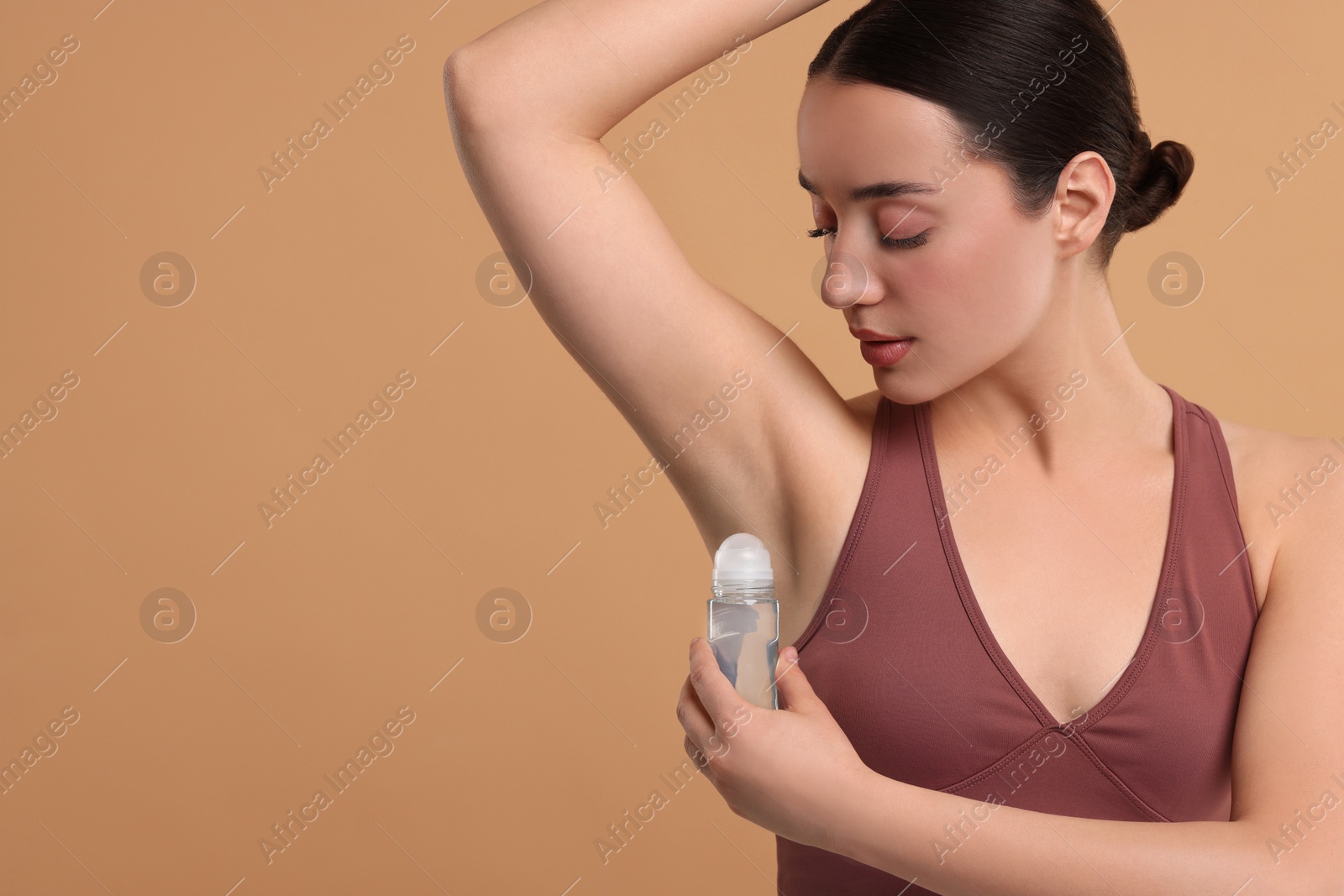 Photo of Beautiful woman applying deodorant on beige background, space for text