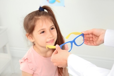 Photo of Female ophthalmologist putting glasses on little girl in clinic