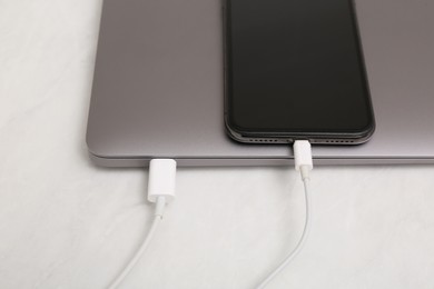 Smartphone connected with charge cable to laptop on light table, closeup